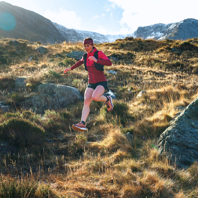 A trail runner in a red jacket running down a grassy mountain hill