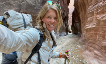 A woman with blonde hair in a white jacket taking a selfie in a slot canyon