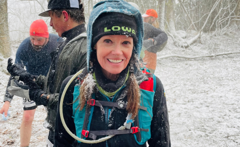 Woman runner smiling in the snow with a LOWA hat, hoodie and hydration vest