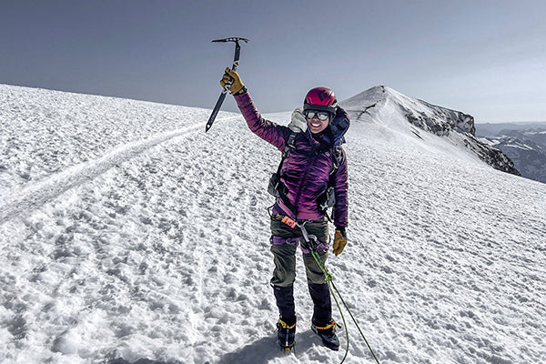 Woman in purple jacket and helmet holding ice axe on a snowy mountain peak