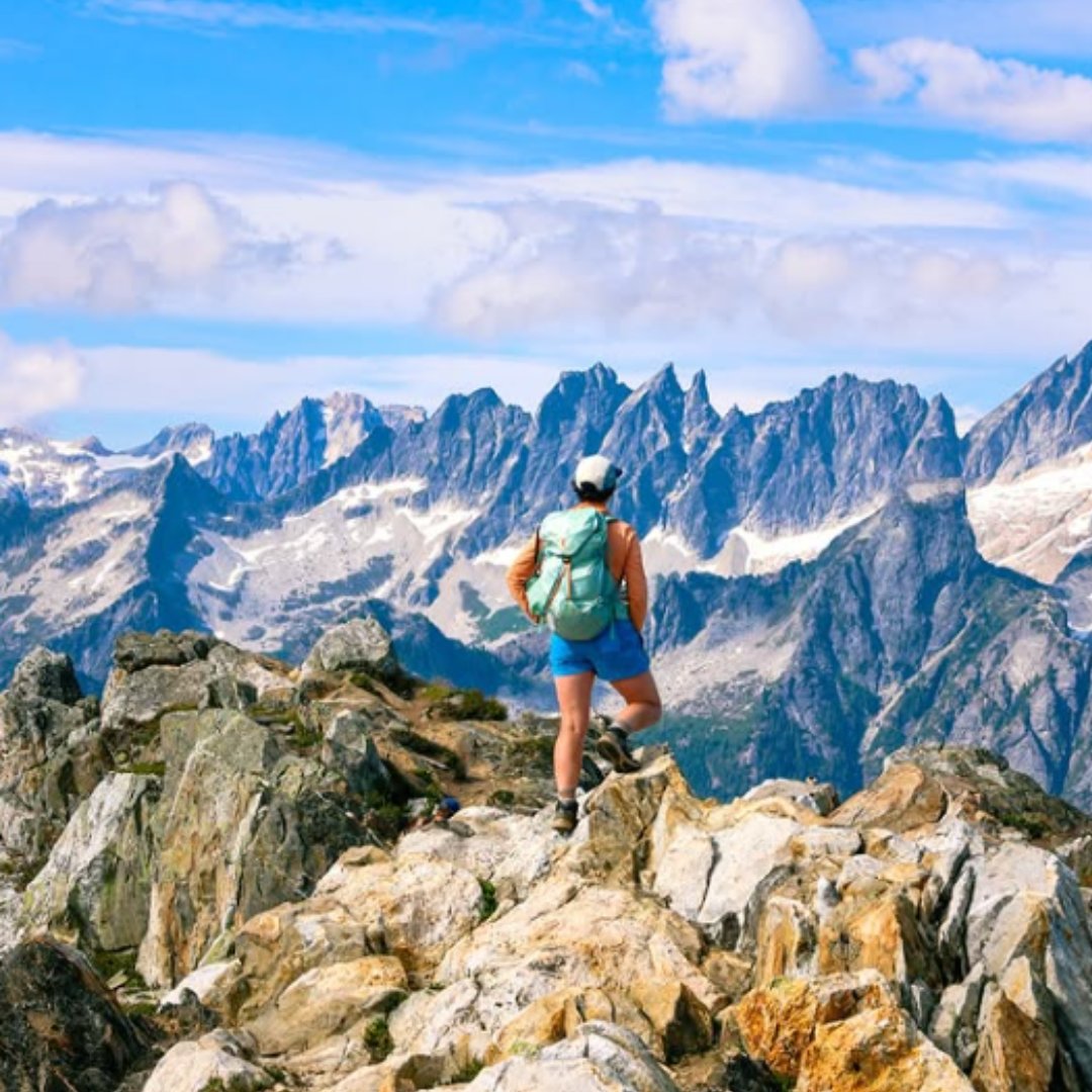 A hiker at the top of a rocky cliff overlooking a jagged mountain range