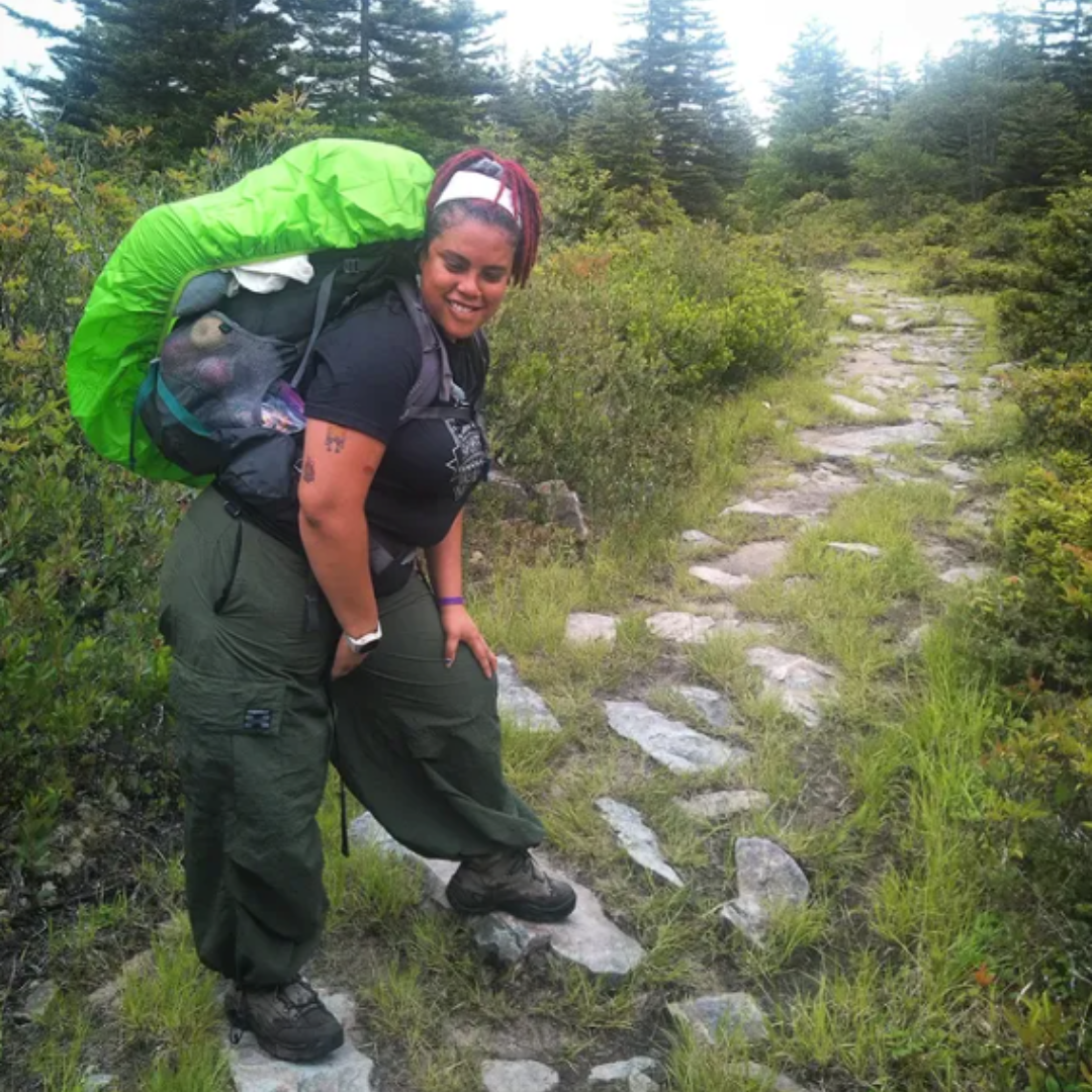 A hiker bent over and smiling on a grassy rocky path in the forest.