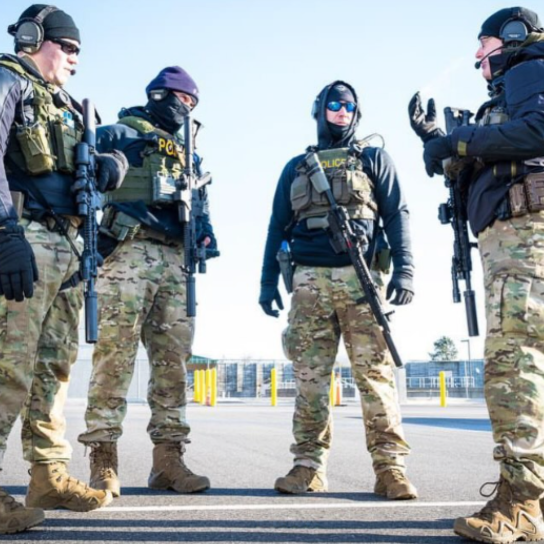 A group of police officers in camo talking in a semicircle