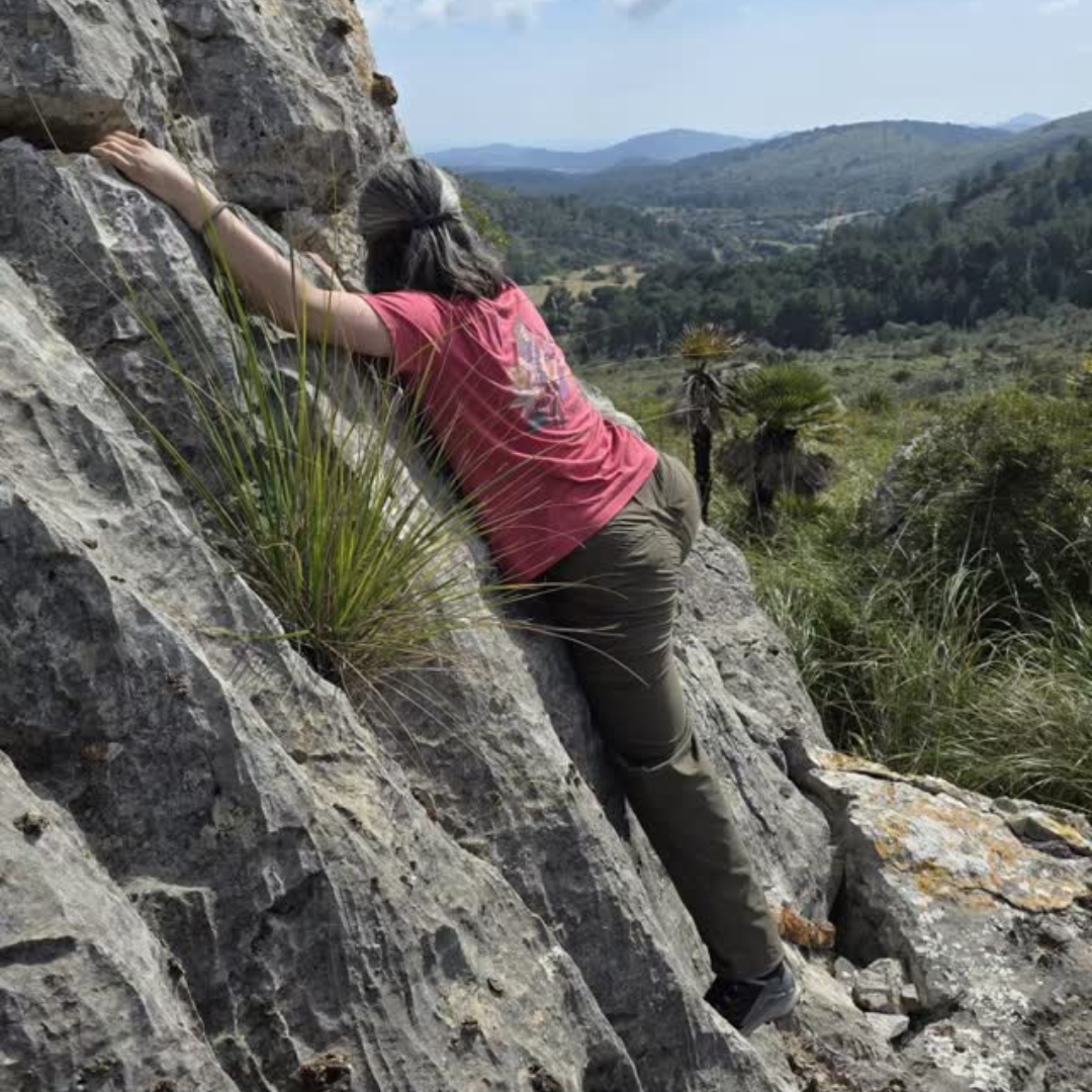 A person hugs the a large boulder in a grassy desert landscape
